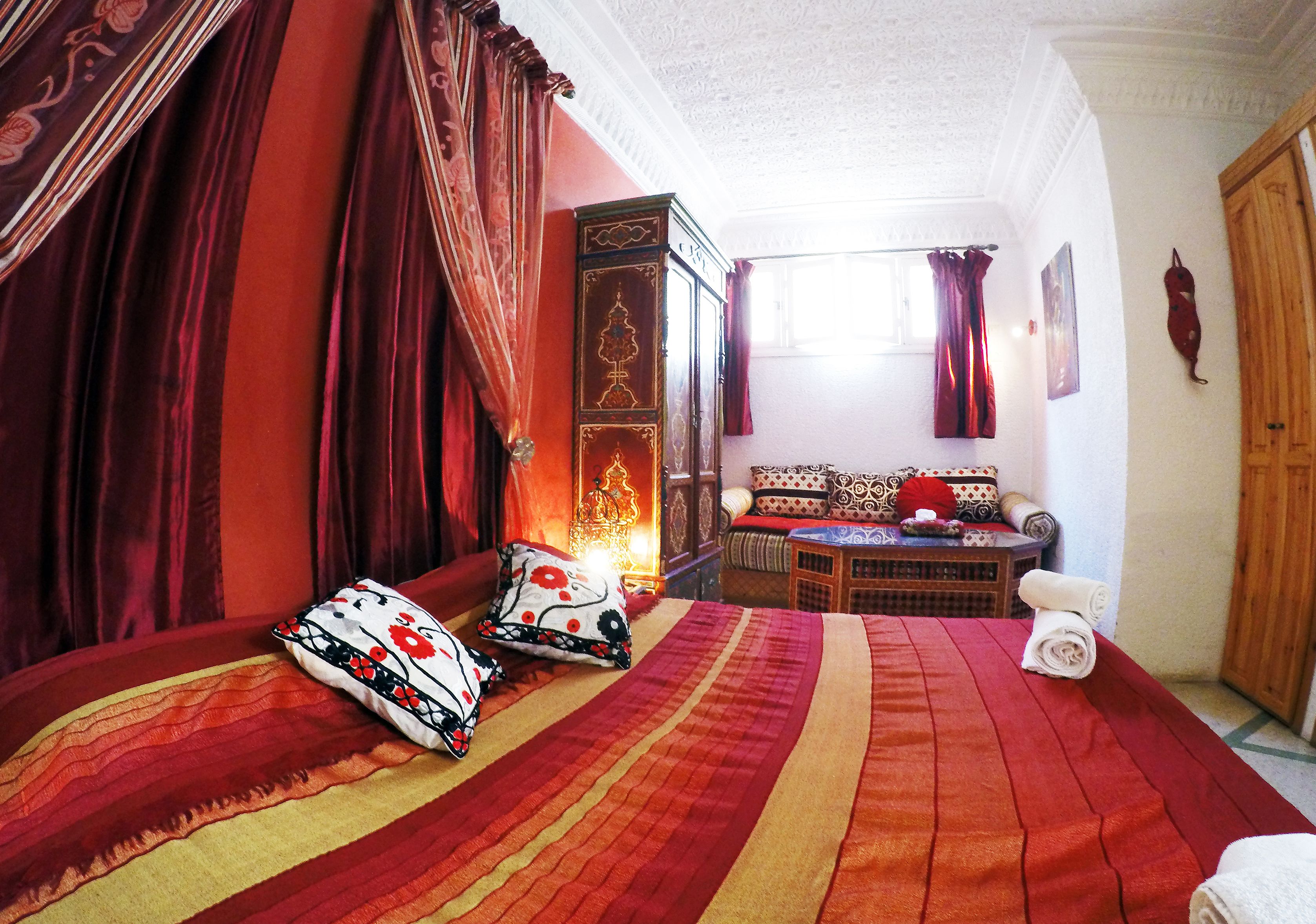 Une pièce comprenant un grand lit, une armoire en bois, un canapé et une fenêtre avec des rideaux.