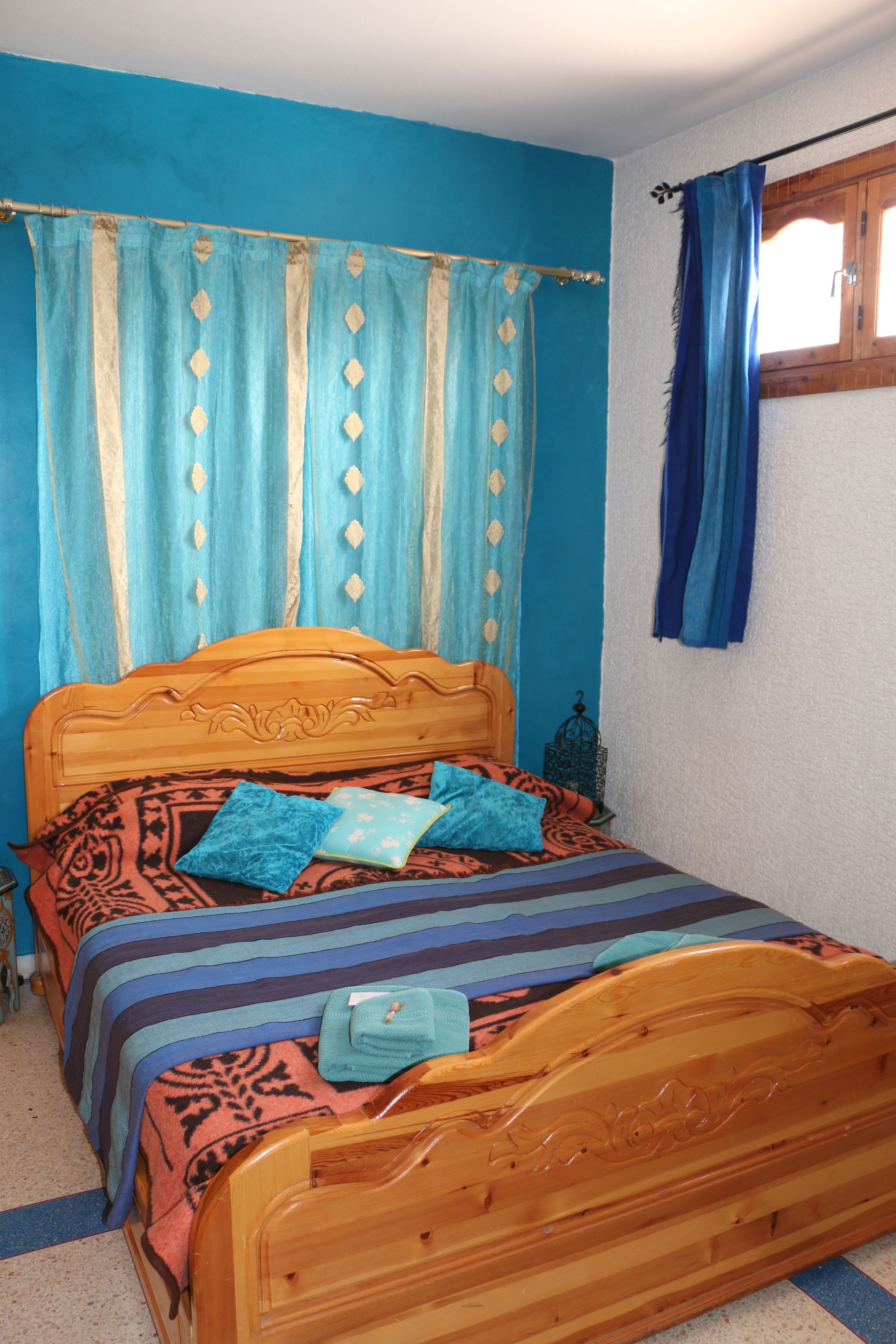 A bedroom with a wooden bed, blue curtains, and a window with a wooden frame.