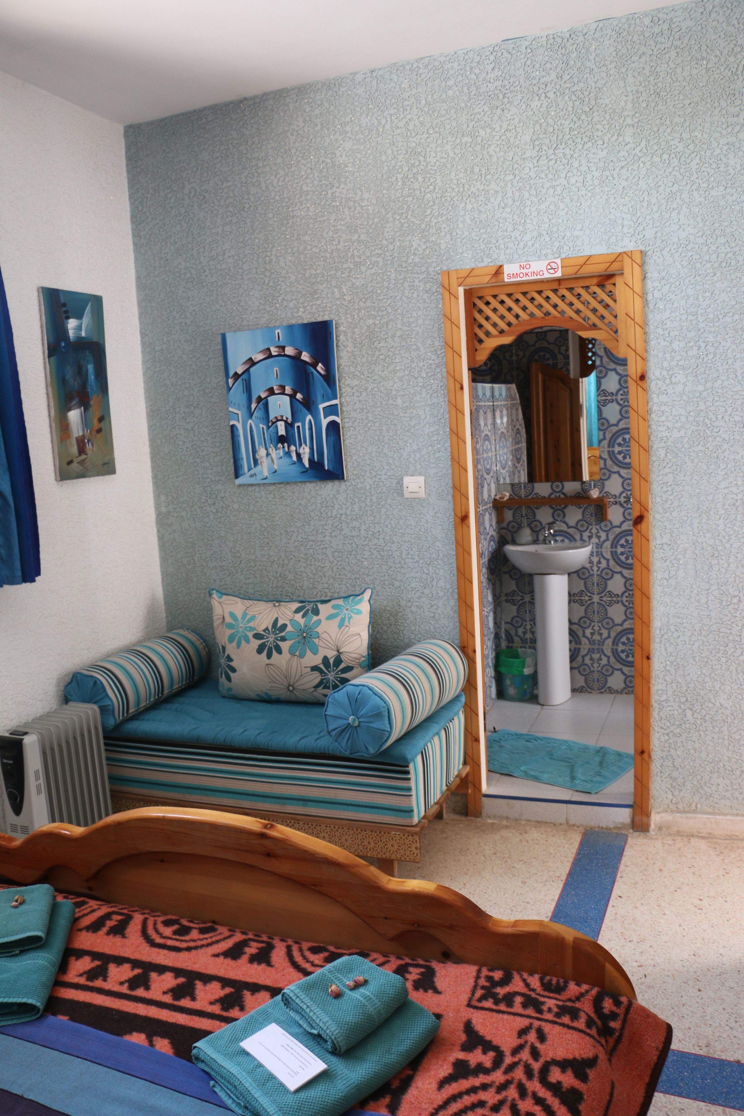 Ein Zimmer mit einer Couch, einem Bett, einem kleinen Tisch, einem Wandbild, einem Spiegel und einer Tür zu einem Badezimmer.