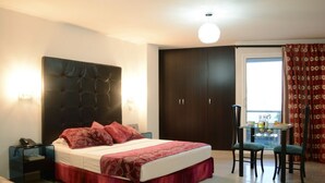 A bedroom with a large bed, a bedside table, a chair, a small table with a lamp, and a wardrobe. - Hotel Calima Real (Cali)