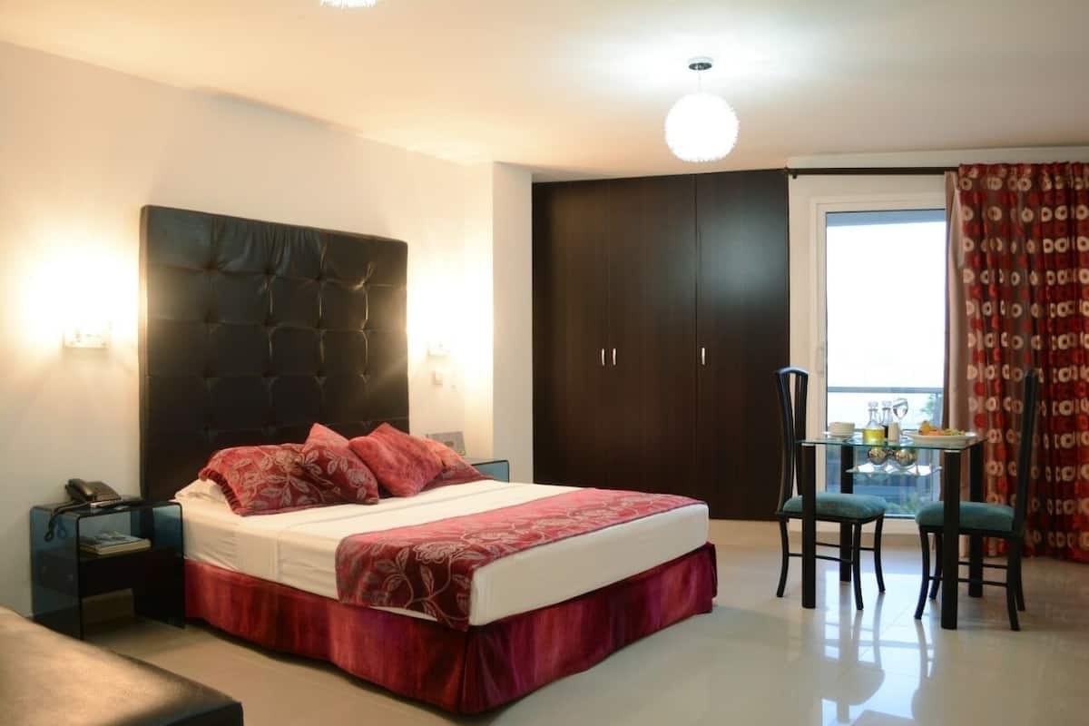 Een slaapkamer met een groot bed, een nachtkastje, een stoel, een klein tafeltje met een lamp en een kledingkast.