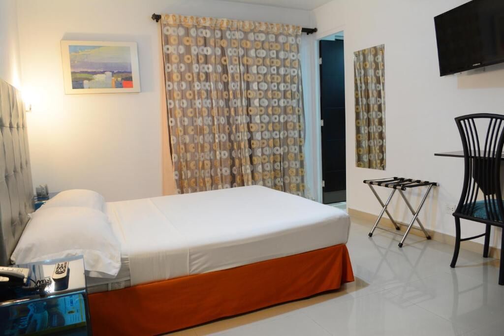 Una habitación de hotel con una cama, una silla, un televisor y un cuadro en la pared.
