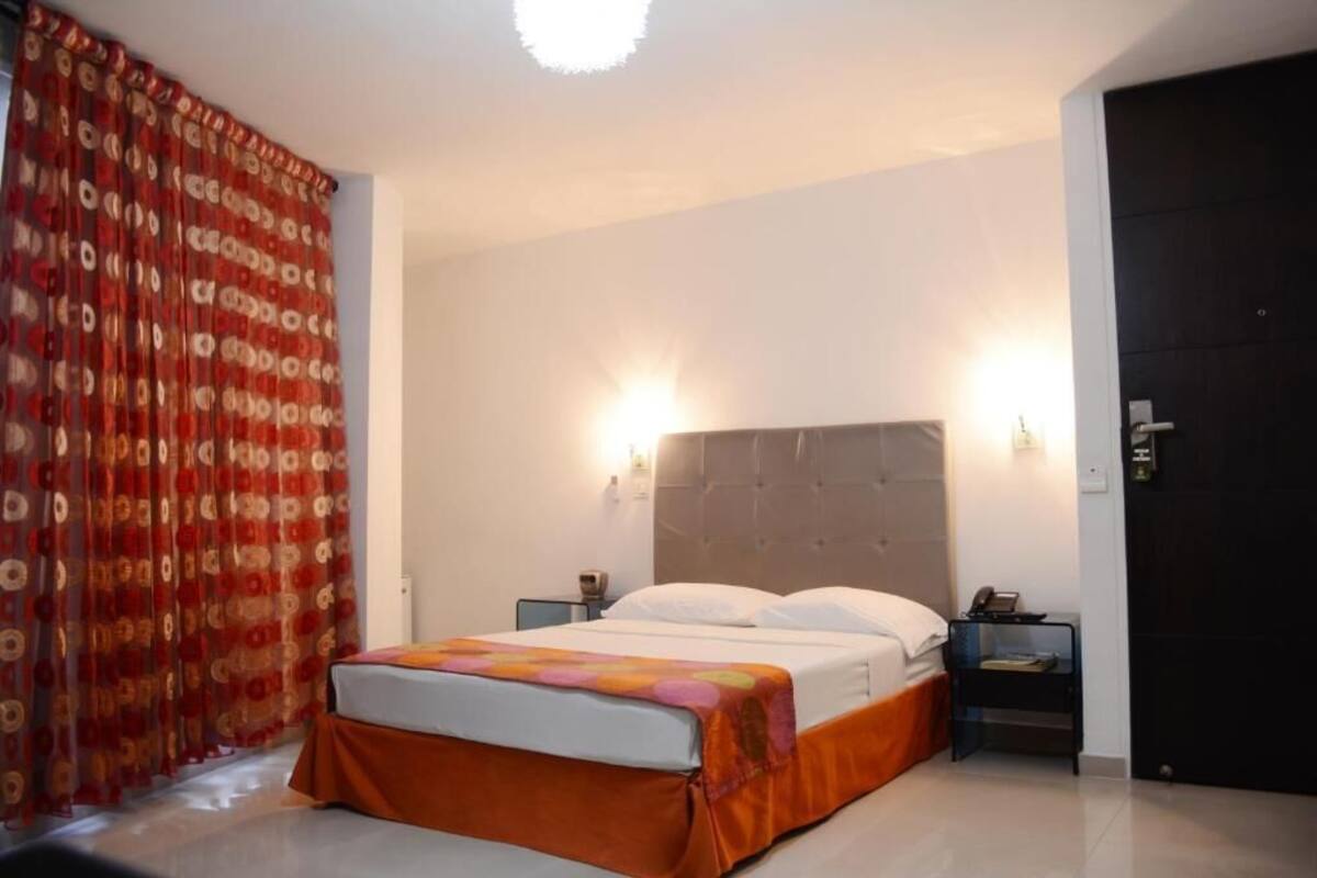 Een hotelkamer met een bed, twee nachtkastjes, een deur en een gordijn.