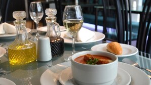 A dining table with a bowl of soup, a glass of white wine, and a bottle of olive oil. - Hotel Calima Real (Cali)