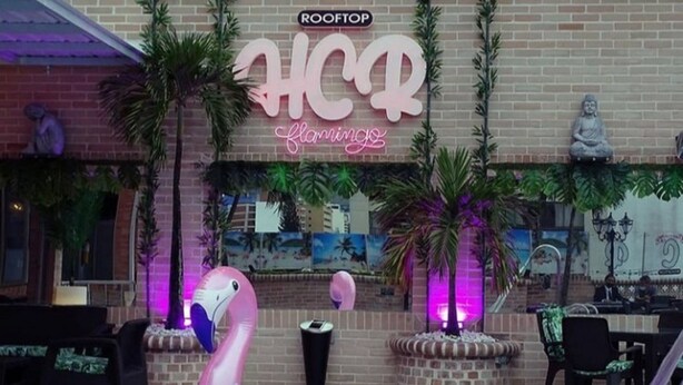 A rooftop bar with flamingo-themed decorations, including a flamingo float and a neon sign. - Hotel Calima Real (Cali)