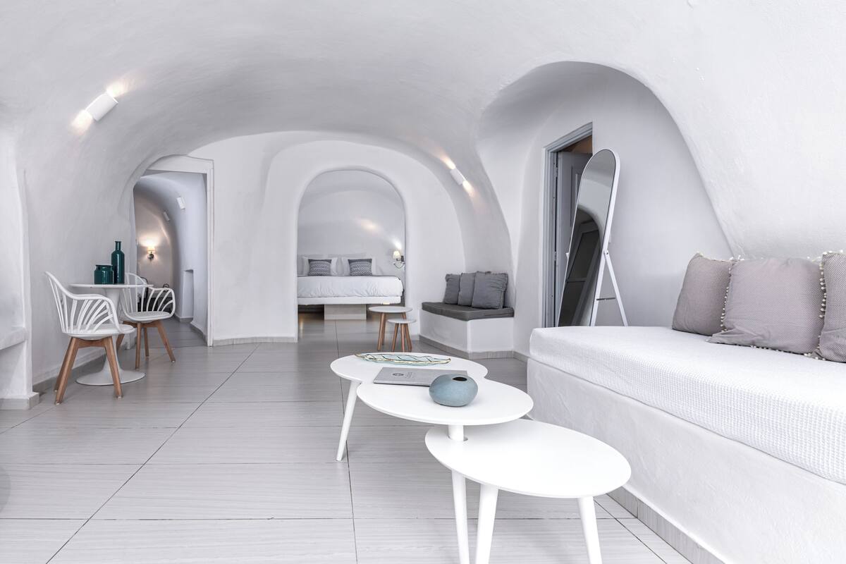 A modern, white-themed living room with a sofa, two small tables, and a dining area with chairs.