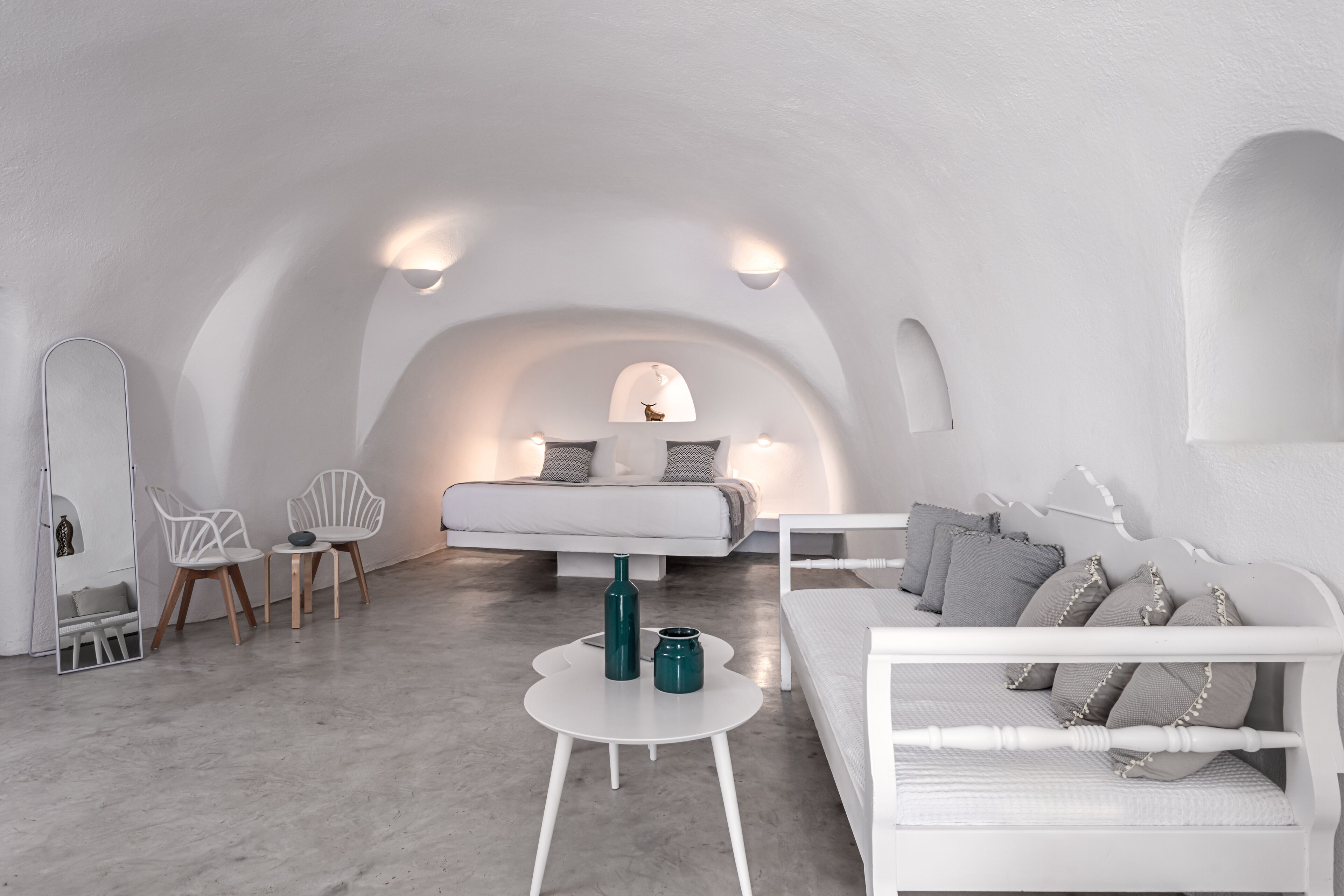 A minimalist, white-themed bedroom with a bed, bedside tables, and seating area.