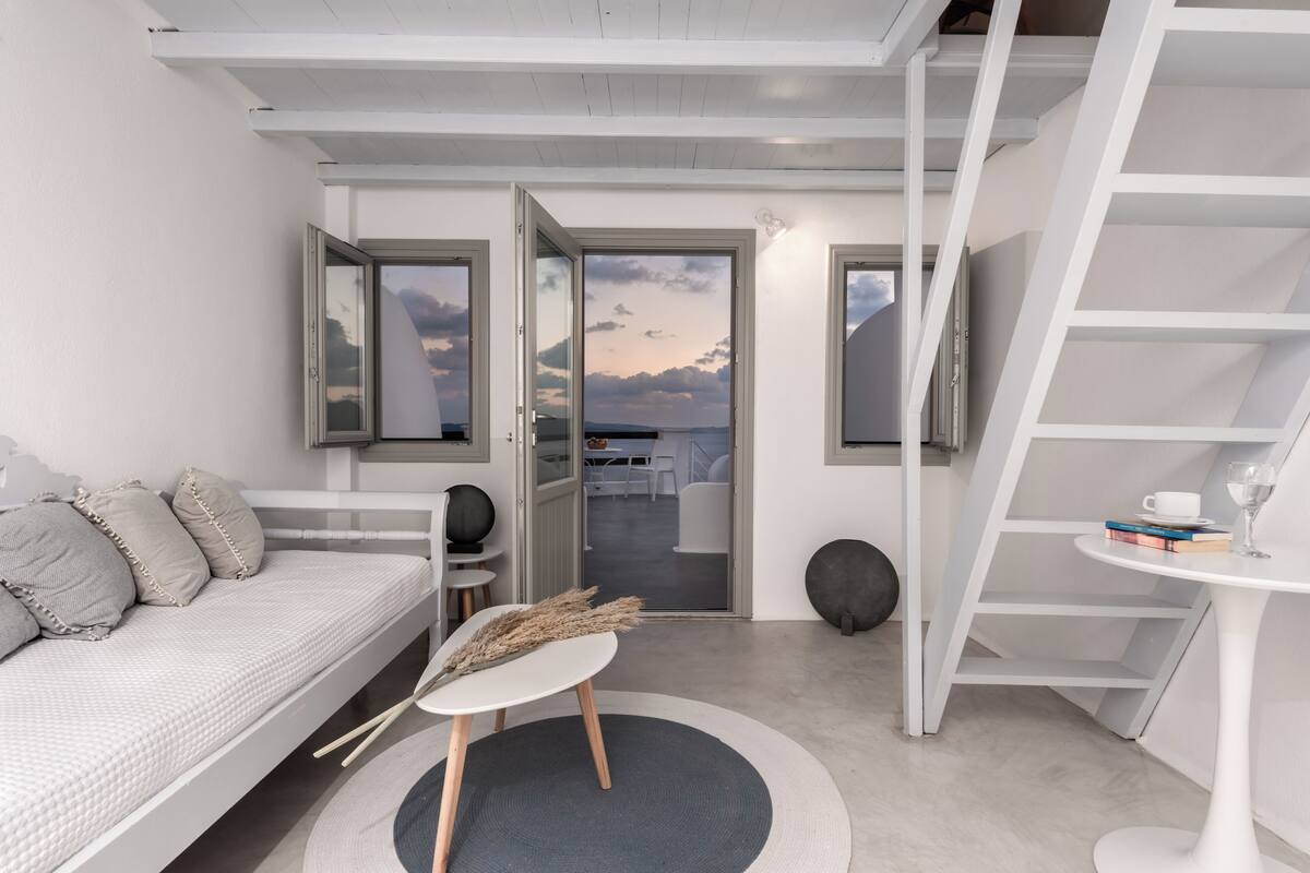 A modern bedroom with a bed, a small table with a vase, a chair, and a view of the outside.