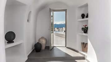 Un pasillo con vista a una terraza exterior, paredes blancas y algunos objetos decorativos en estantes.