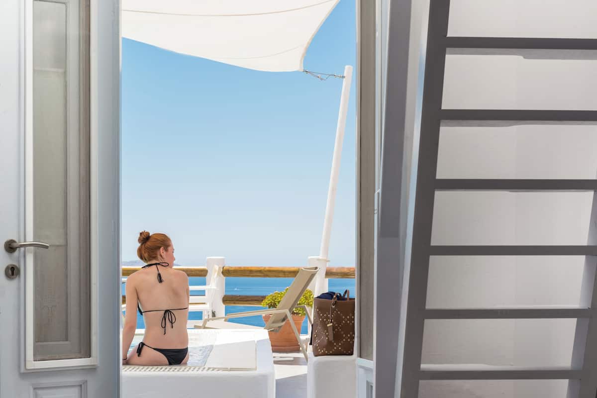 A room with a view of the sea, a door, a chair, and a table.