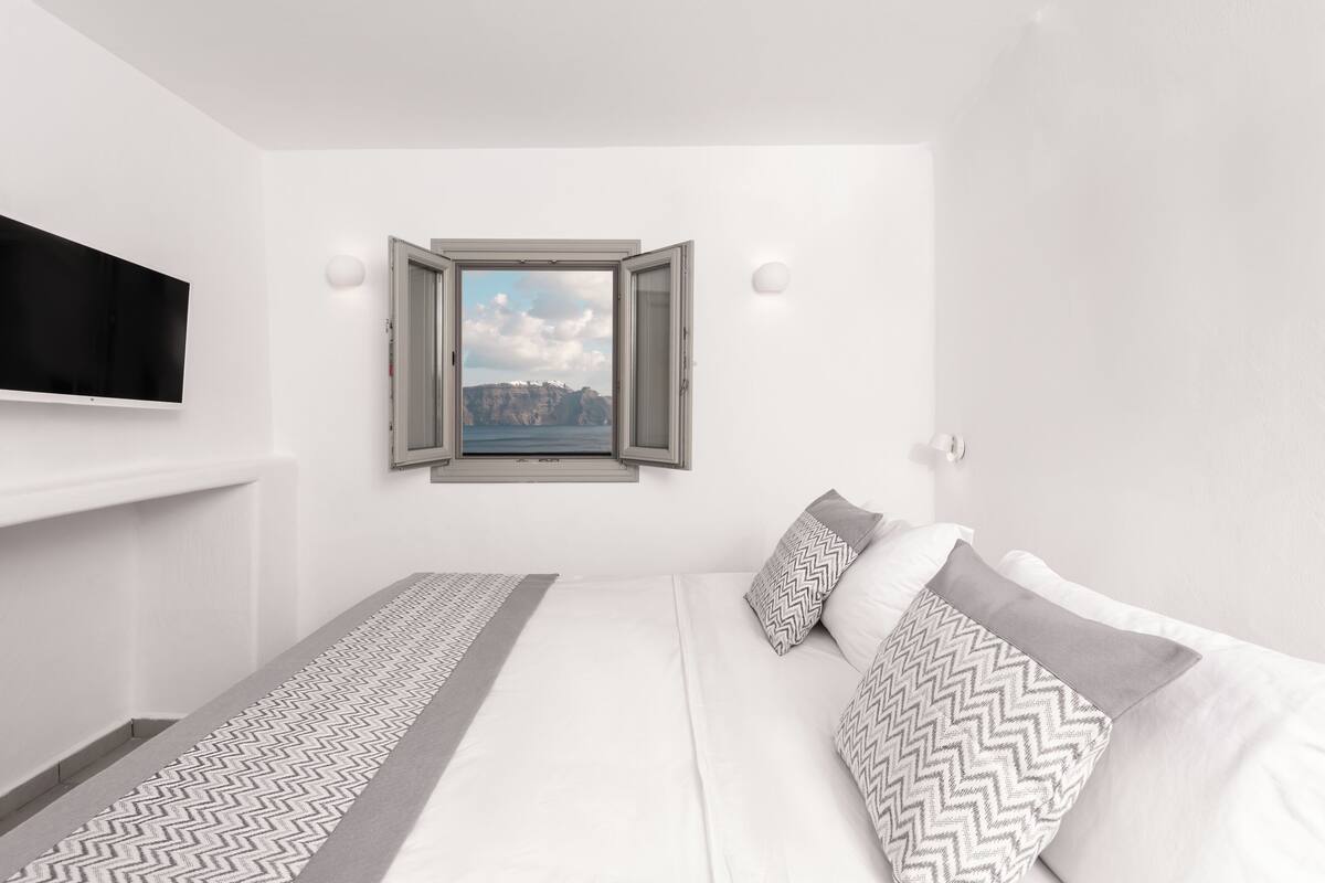 A modern bedroom with a bed, a TV, a window with a view of cliffs, and a patterned runner.