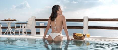 Eine Frau im Pool, in der Nähe ein Tisch und Stühle, mit Blick auf ein Gewässer.