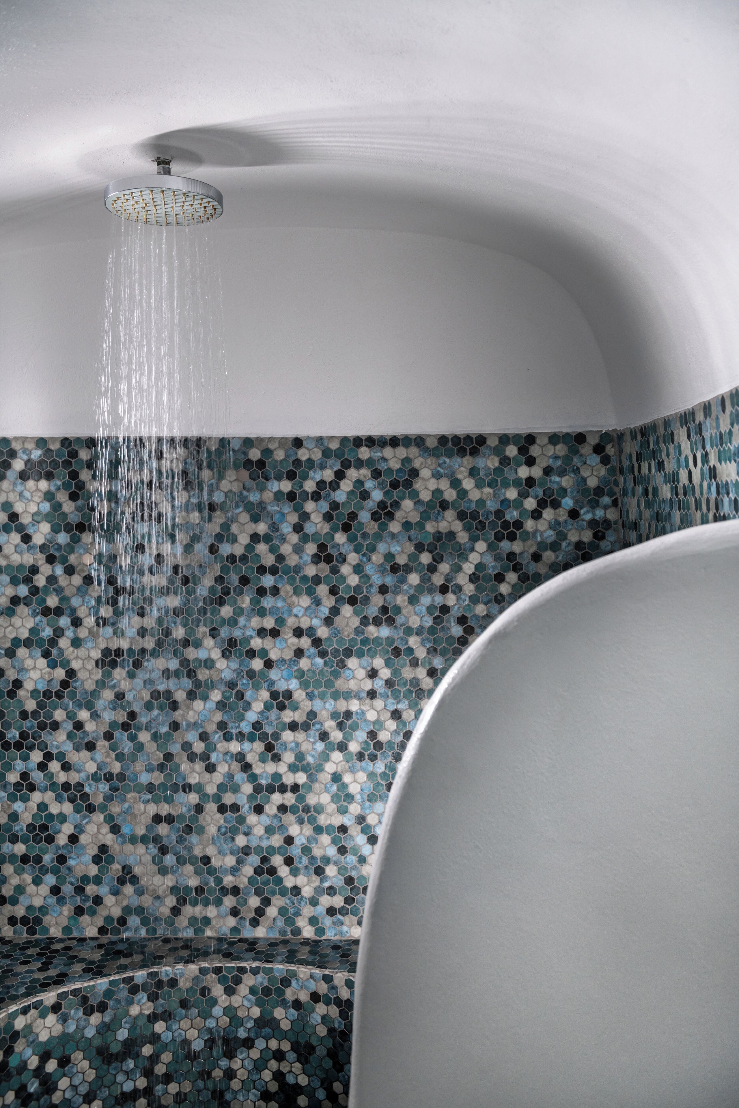 A shower with a mosaic tile wall and a white bathtub.