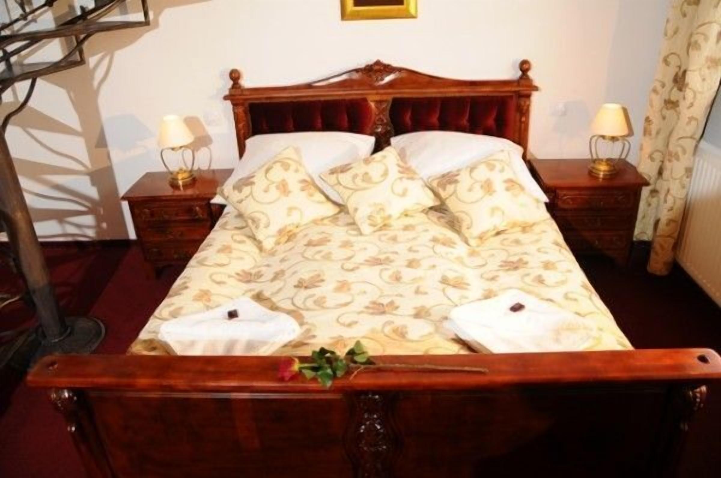 A wooden bed with a floral bedspread and matching pillows, two bedside lamps, and a small plant on the bed.
