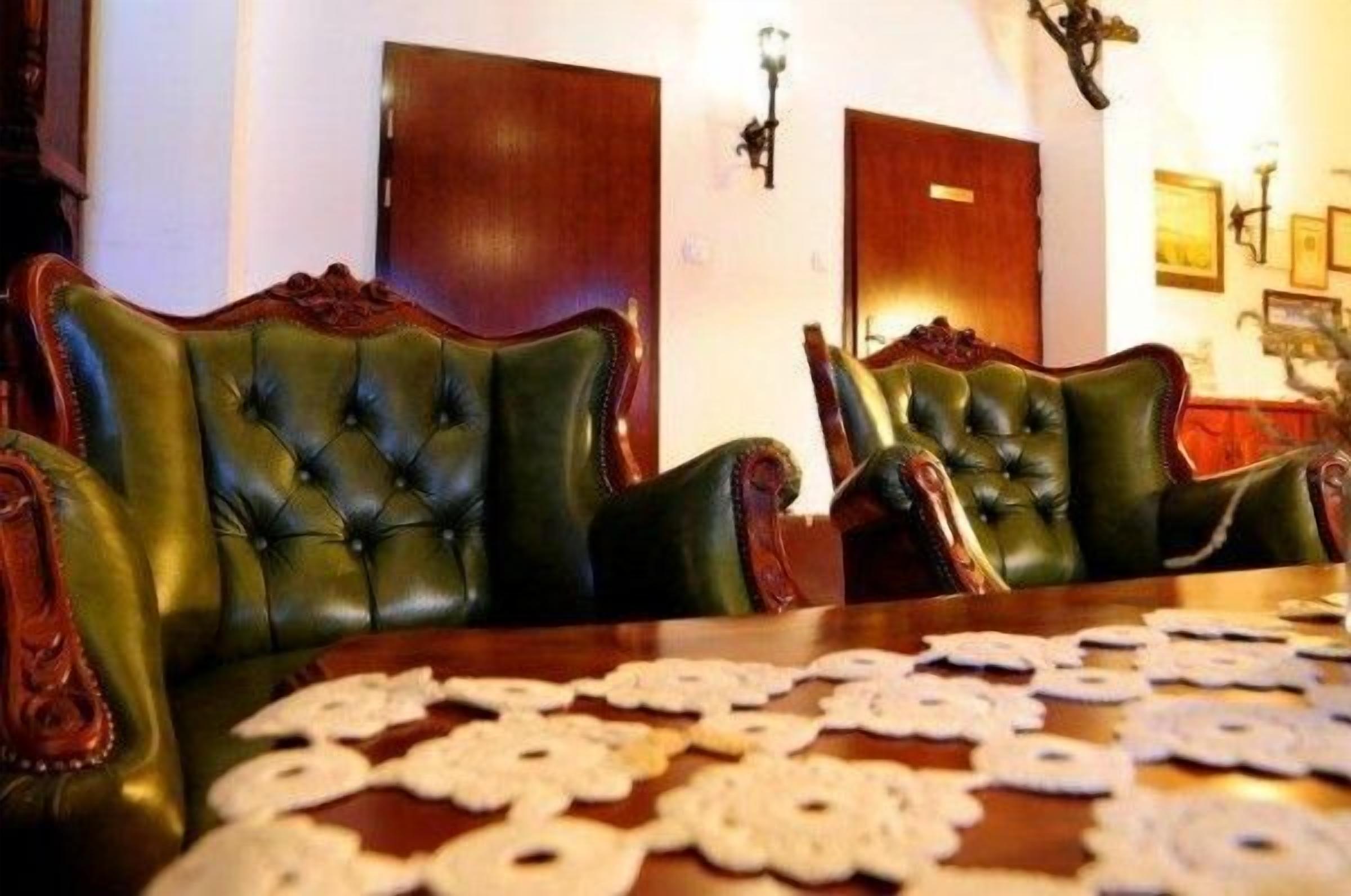 A room with a wooden table, green leather chairs, and a lace tablecloth.