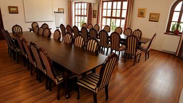 Un salón de conferencias con una larga mesa de madera y sillas a rayas, ventanas amplias con cortinas y cuadros en las paredes.