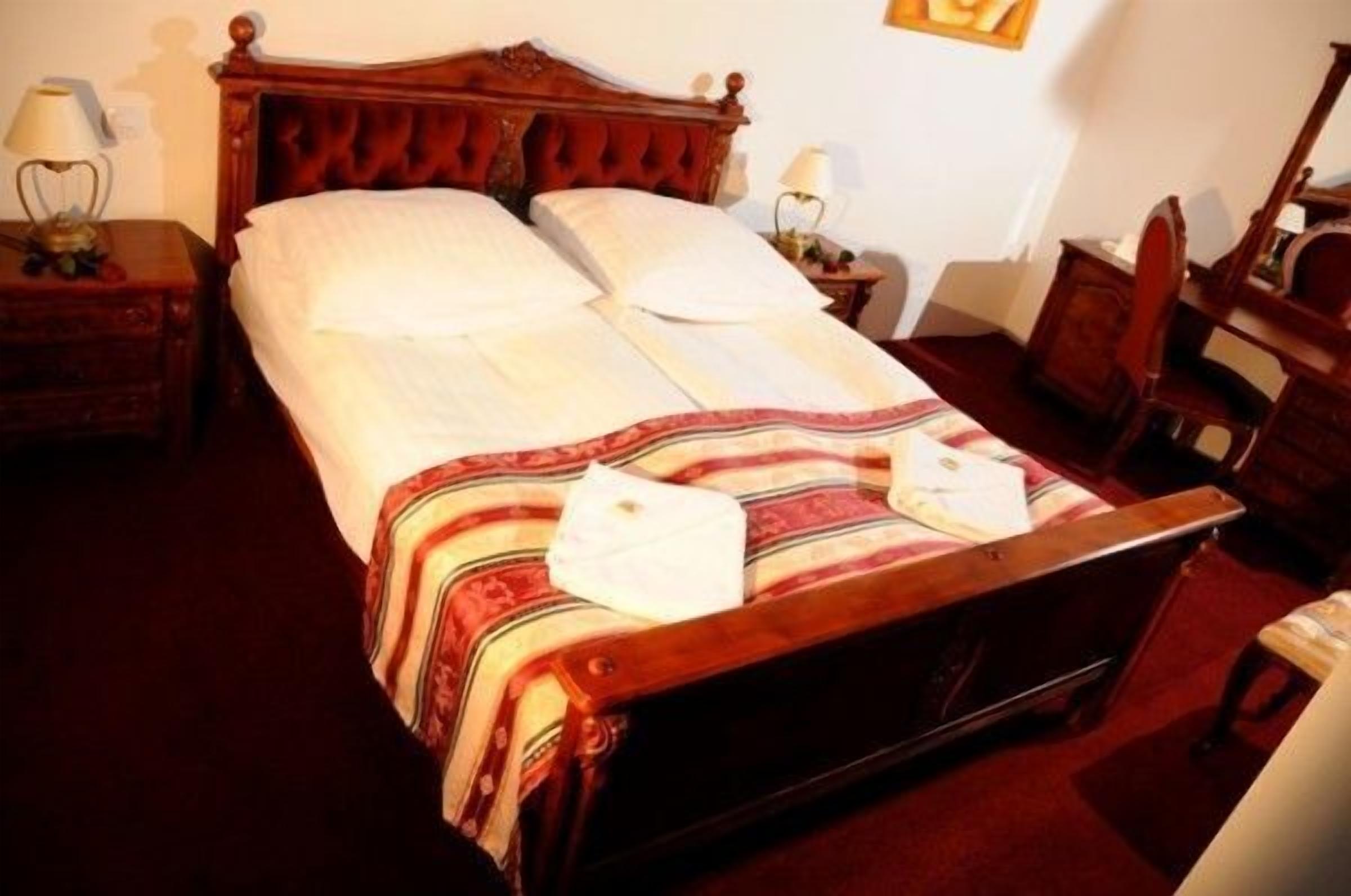 Una cama bien hecha con una manta a rayas y almohadas, cabecera de madera, mesitas de noche con lámparas y una silla.