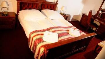 Una cama bien hecha con una manta a rayas y almohadas, cabecera de madera, mesitas de noche con lámparas y una silla.