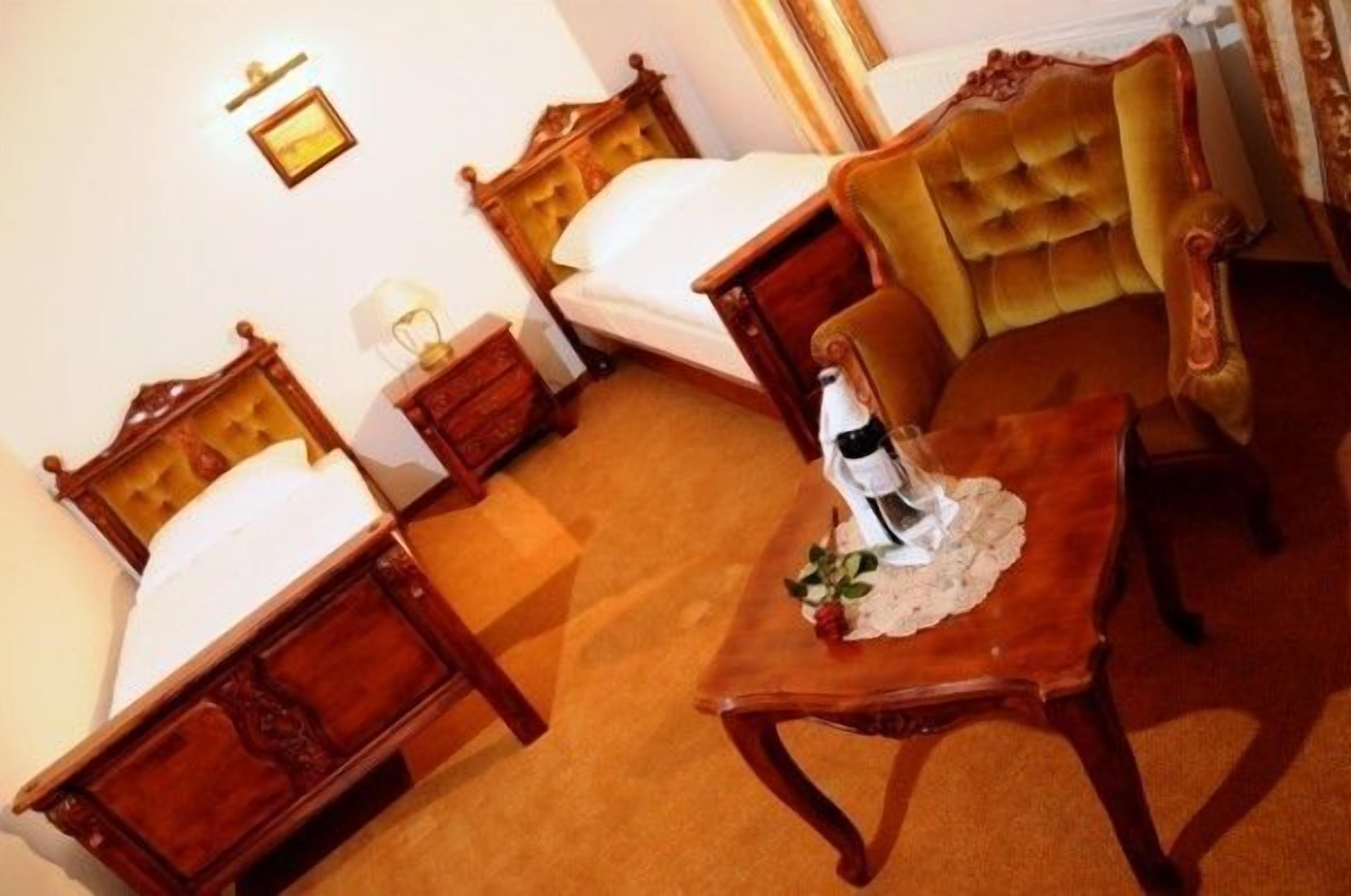 Ein Hotelzimmer mit zwei hölzernen Betten, einem komfortablen Sessel und einem kleinen Tisch mit einer Flasche und einer Blume.