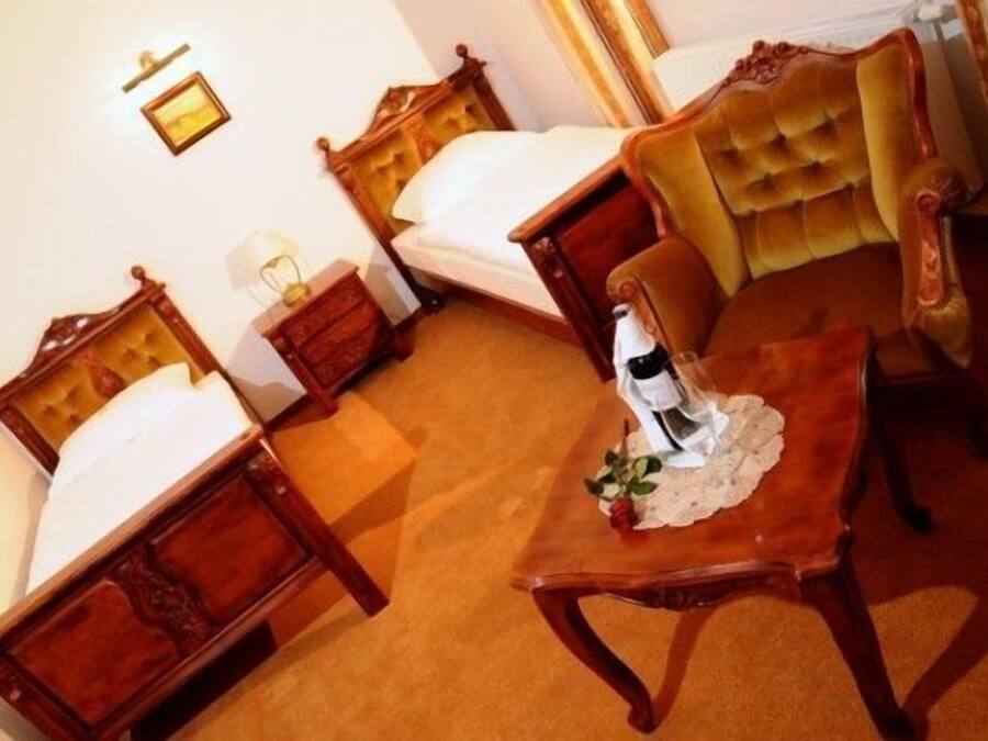 Habitación de hotel con dos camas de madera, un sillón mullido y una mesita con una botella y una flor.