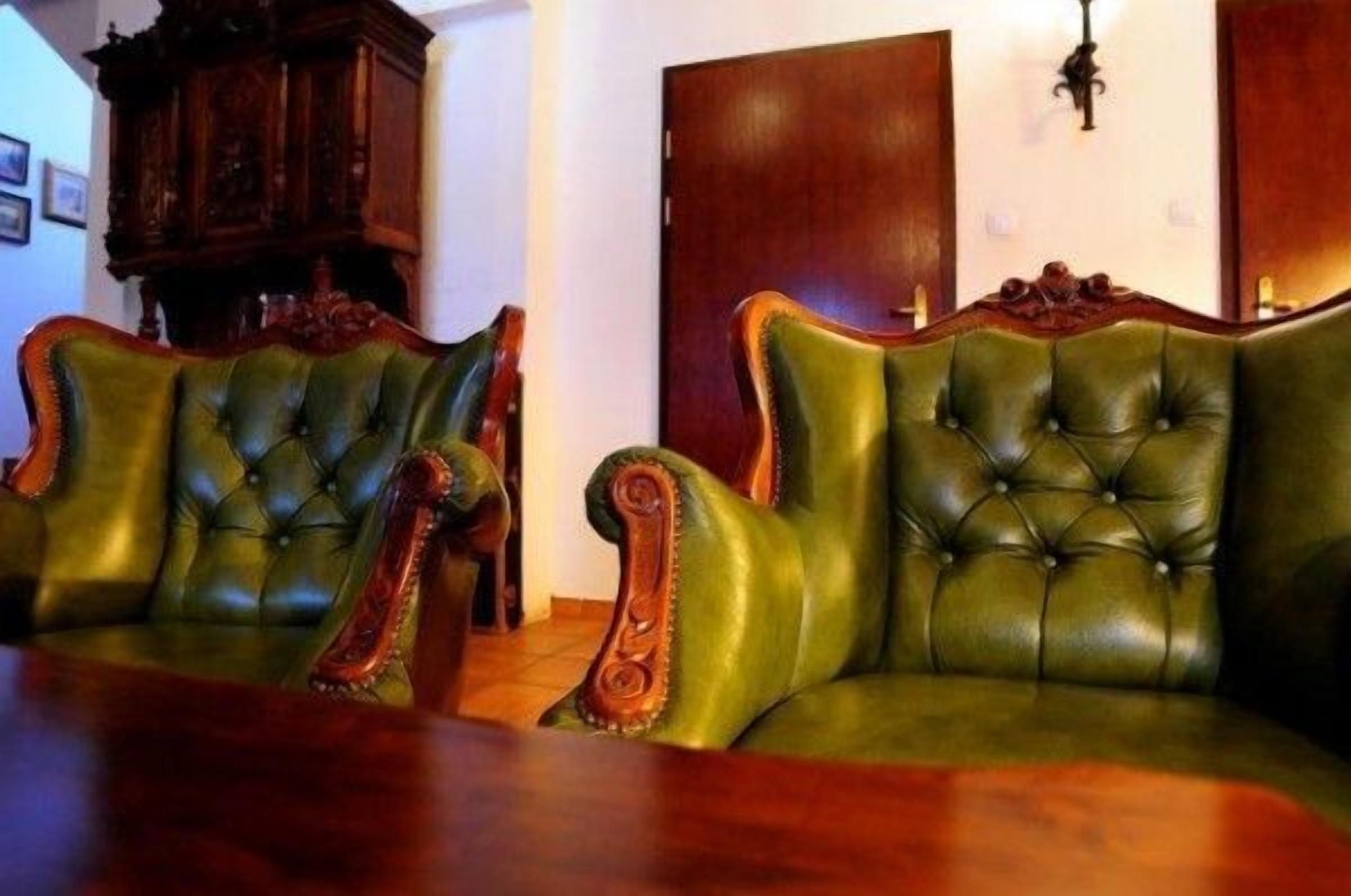 Une pièce comprenant deux fauteuils à accoudoirs recouverts d’un tissu vert, avec un dossier capitonné et des accoudoirs en bois, ainsi qu’un meuble et une porte en bois.
