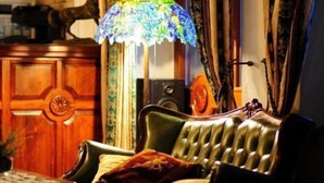 Una habitación de estilo vintage con un sofá de cuero, un armario de madera y una lámpara de vitral colorida.