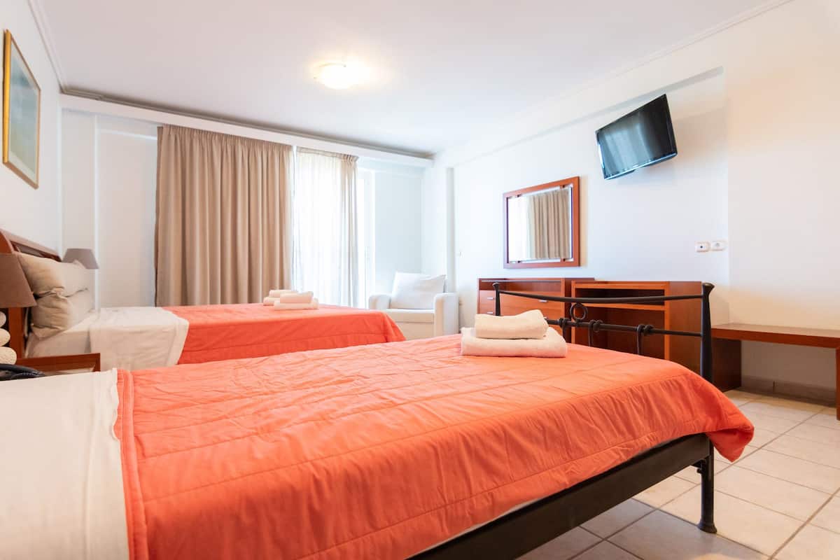 Habitación de hotel con dos camas, un escritorio, una silla, un televisor y un ventanal con cortinas.