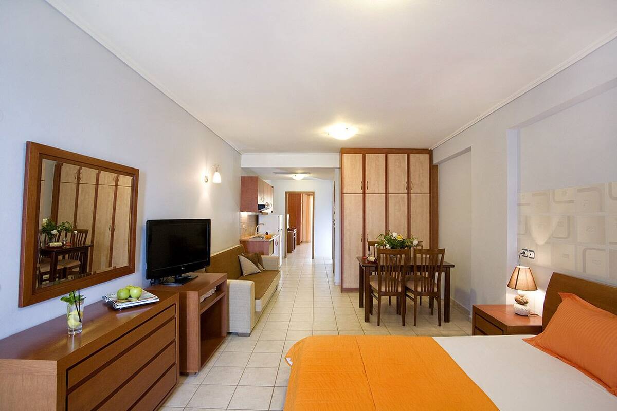Habitación de hotel con cama, televisor, escritorio, silla, mesa de comedor y espejo.