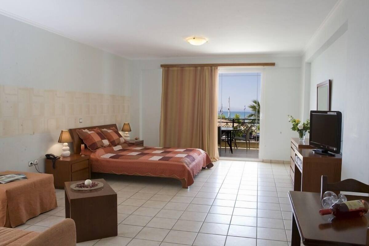 Una habitación de hotel con cama, televisión, mesa de comedor y balcón con vistas.