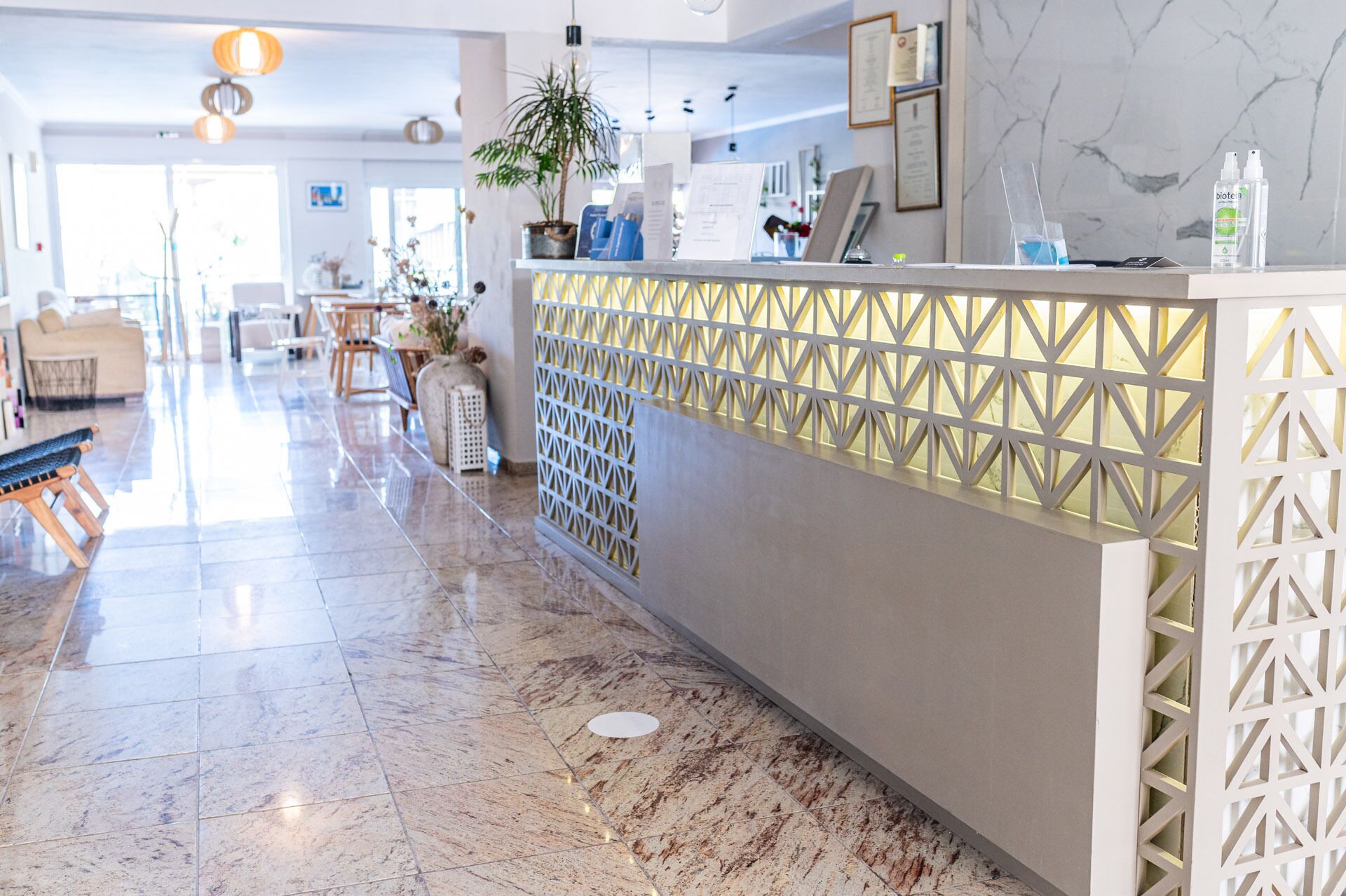 A hotel reception area with a marble floor, a reception desk with a geometric patterned partition, and a seating area with sofas and a coffee table.