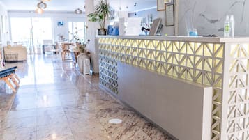 A hotel reception area with a marble floor, a reception desk with a geometric patterned partition, and a seating area with sofas and a coffee table.