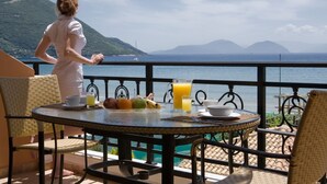 Un balcón con una mesa dispuesta para el desayuno, con vistas panorámicas del mar y las montañas.