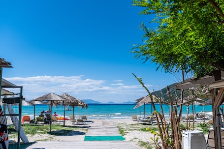 A beach with thatched umbrellas, lounge chairs, and a wooden walkway leading to the sea.