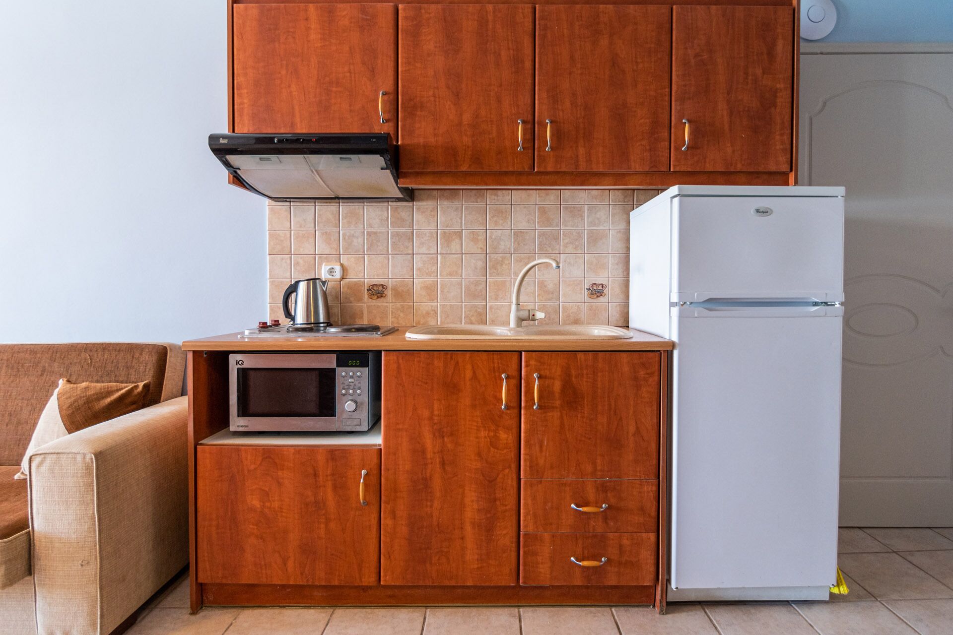 Una cocina compacta con armarios de madera, microondas integrado, un lavamanos y un refrigerador blanco.