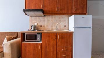 Una cocina compacta con armarios de madera, microondas integrado, un lavamanos y un refrigerador blanco.