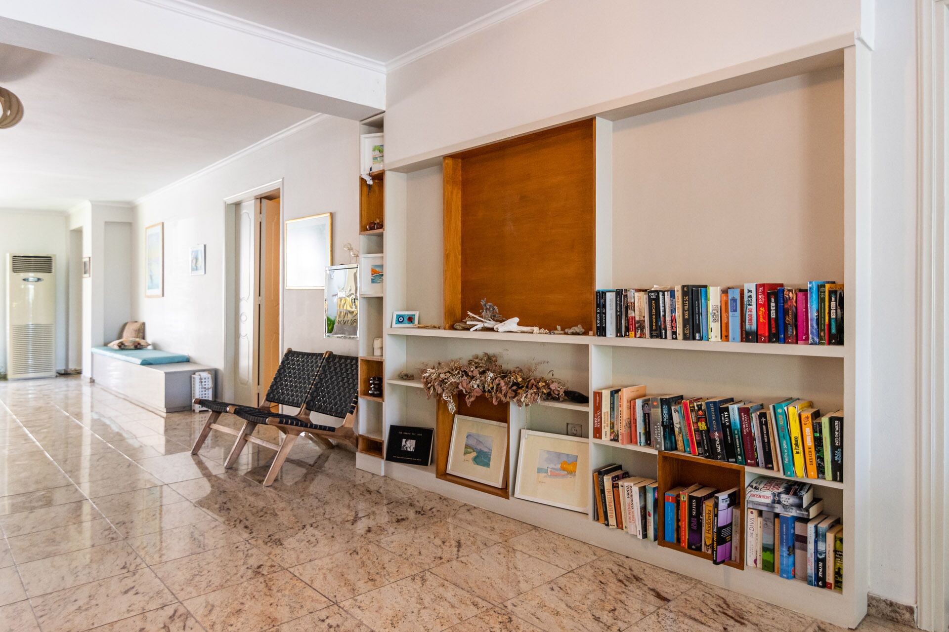 Un couloir avec une bibliothèque remplie de livres, un banc avec des coussins et une chaise fixée au mur.