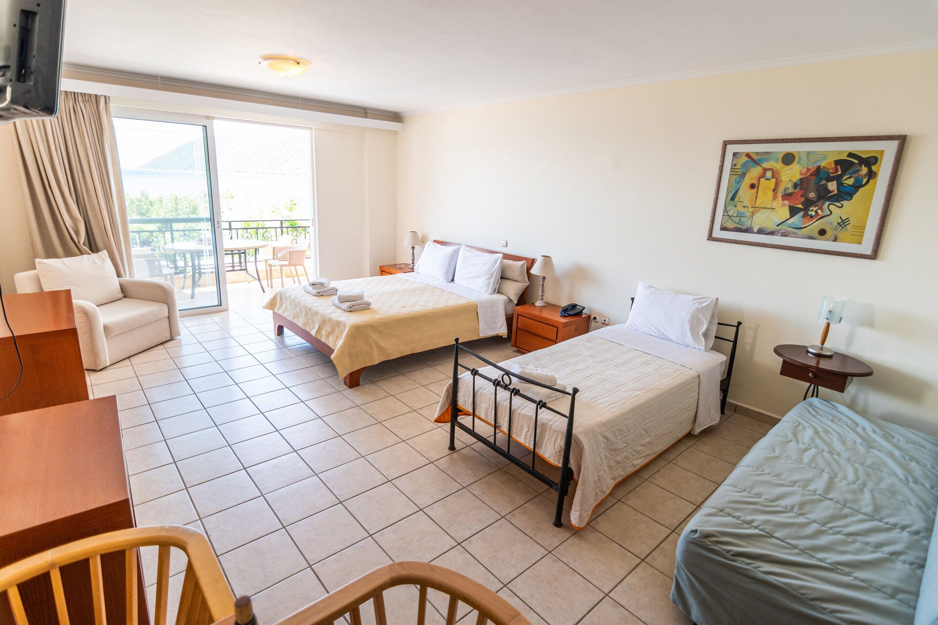 A hotel room with two beds, a sofa, a dining table, and a balcony with a view.