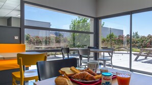 Une table avec des croissants, un verre de jus de fruits et un pot de yaourt, le tout disposé dans un intérieur lumineux et spacieux, avec de grandes fenêtres.