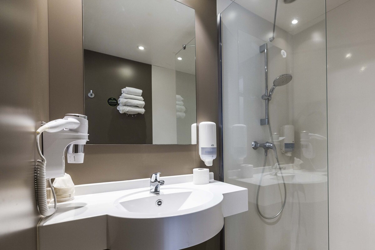 A modern bathroom with a white sink, a mirror, a glass shower enclosure, and a towel rack with neatly folded towels.