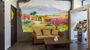 Un hall d’entrée orné d’une fresque représentant un paysage, avec un canapé, une table basse et une étagère où sont exposés des livres.