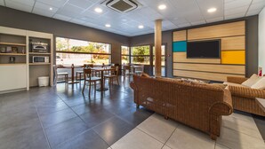 Un espace intérieur spacieux comprenant une table à manger et des chaises, un canapé en osier et un téléviseur à écran plat fixé au mur.