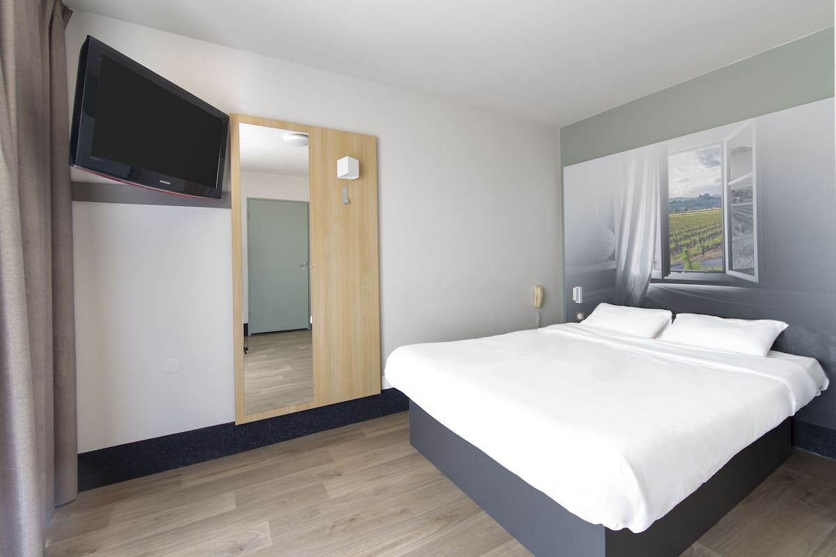 Ein modernes Schlafzimmer mit Bett, einem Flachbildfernseher an der Wand und einem großen Fenster mit Blick auf einen Weinberg.
