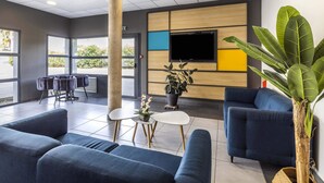 Un hall d’entrée moderne avec des canapés bleus, un téléviseur à écran plat et une plante en pot.