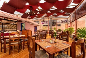 Un restaurante con mesas y sillas de madera, una araña y plantas en macetas.