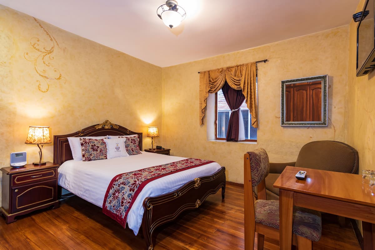 Habitación de hotel con cama de madera, lámparas de noche, un escritorio con silla y una ventana con cortinas.