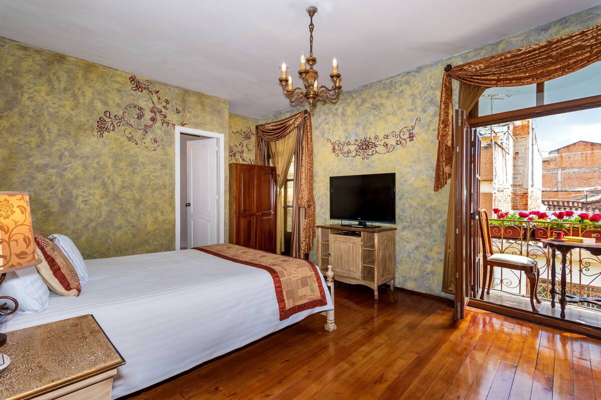 Una habitación de hotel con una cama grande, un escritorio de madera con un televisor y un balcón lleno de flores.