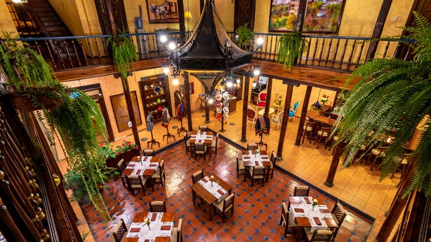 An indoor dining area with multiple tables and chairs, a central chandelier, and hanging plants. - Hotel Boutique Los Balcones (Cuenca)