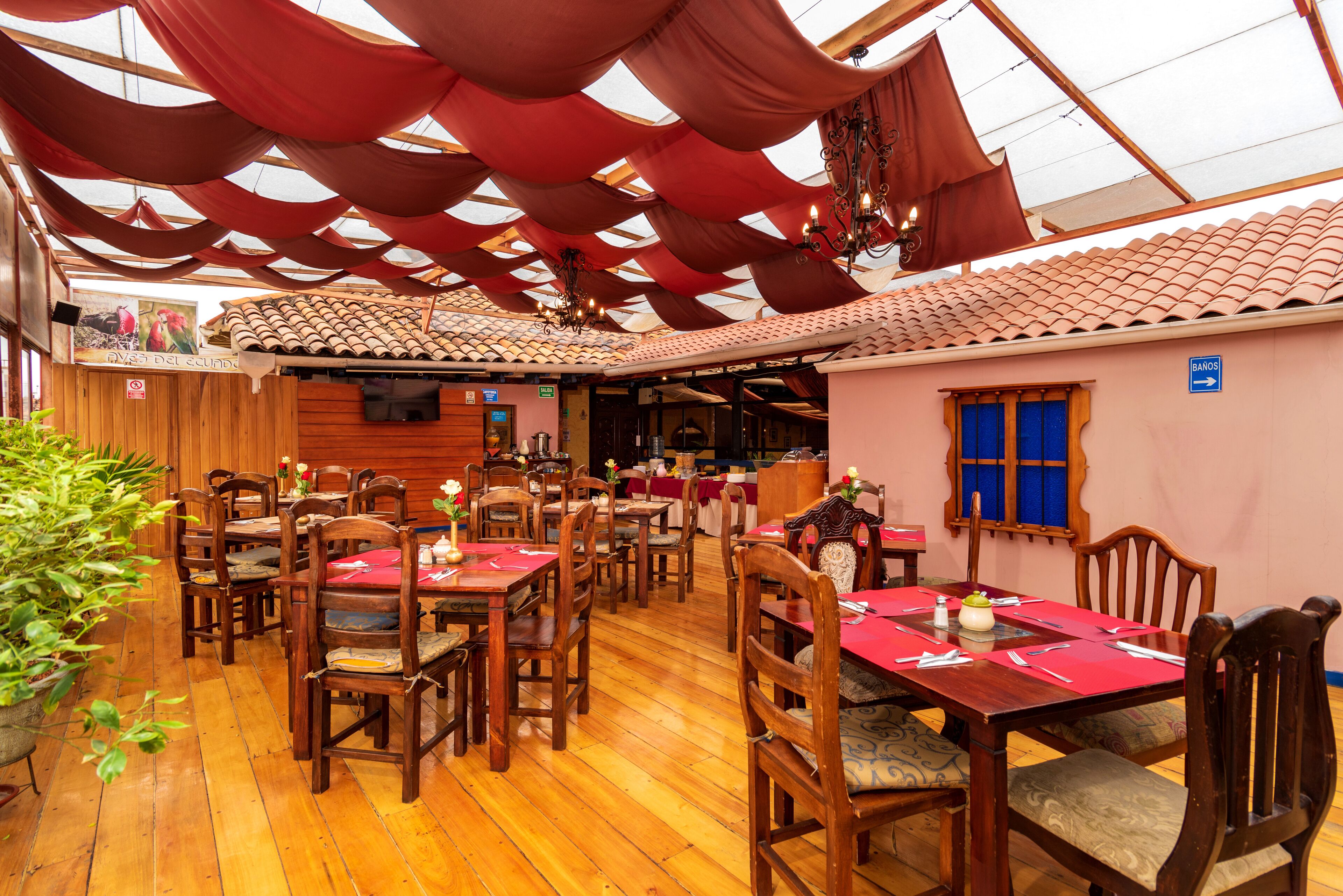 Ein Restaurant mit Holztischen und -stühlen, roten Tischdecken und einer gefliesten Decke.