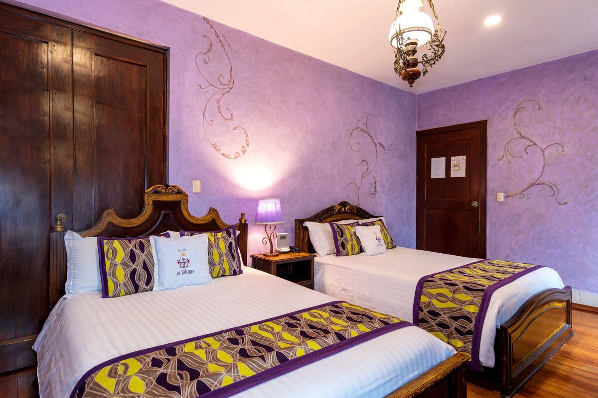 Habitación de hotel con dos camas, paredes moradas y un candelabro.