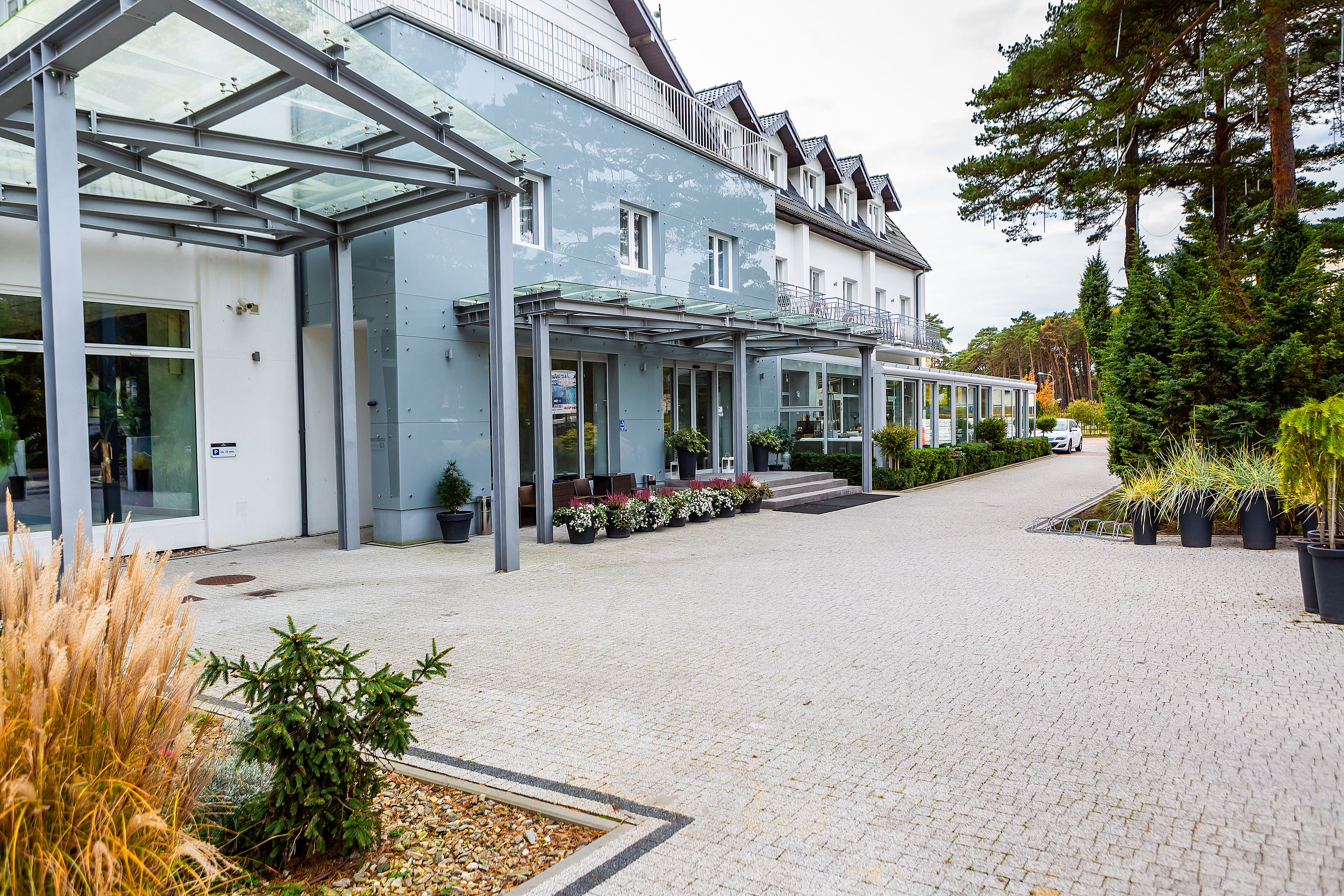 A modern building with a covered entrance, potted plants, and a paved walkway.